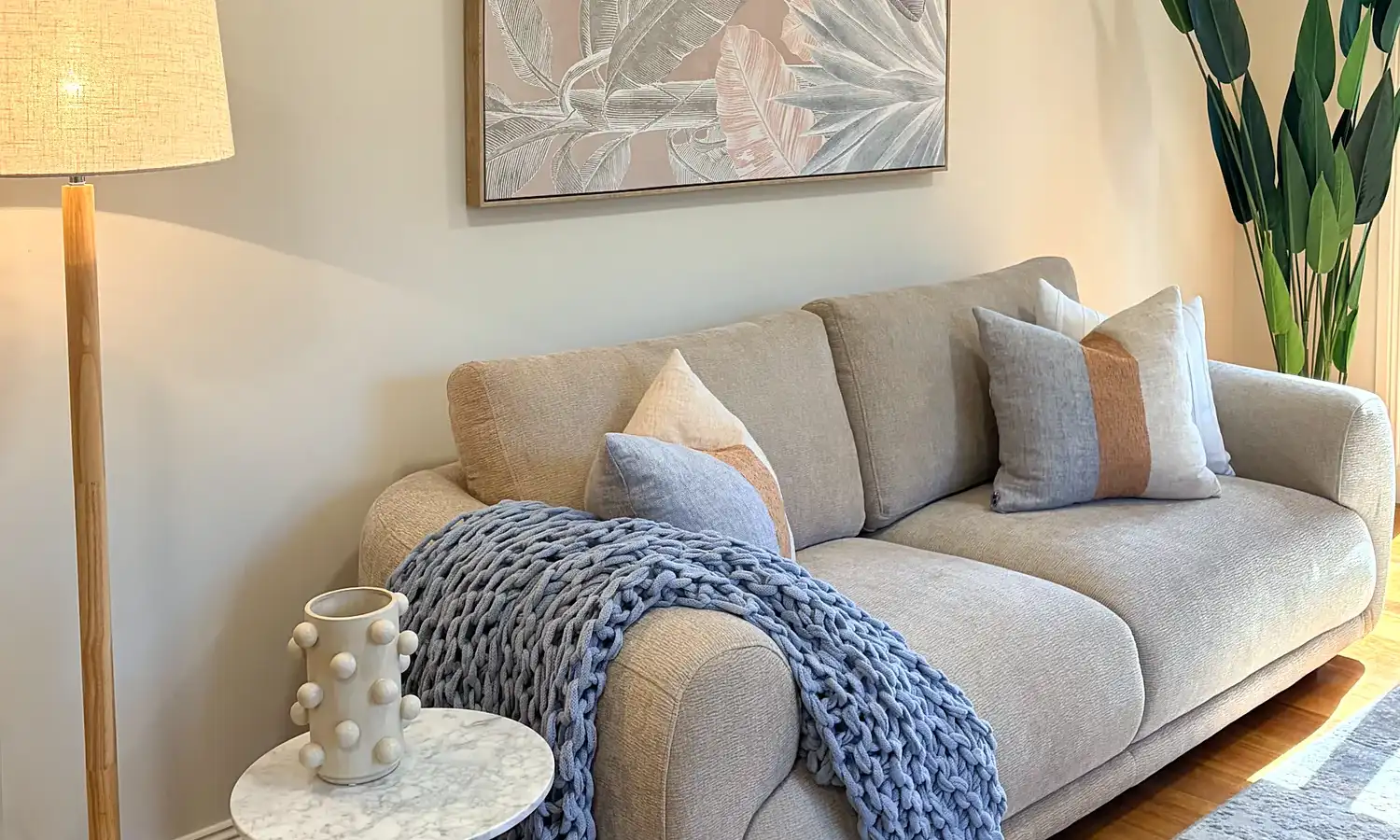 Living room with a grey sofa, chunky blue knit throw, floor lamp and botanical artwork.