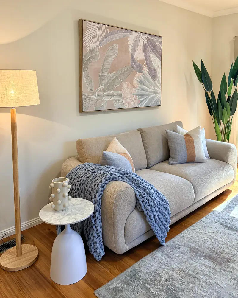 Living room with a grey sofa, chunky blue knit throw, floor lamp and botanical artwork.