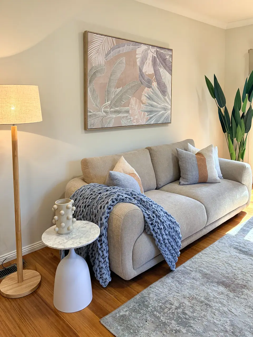 Living room with a grey sofa, chunky blue knit throw, floor lamp and botanical artwork.