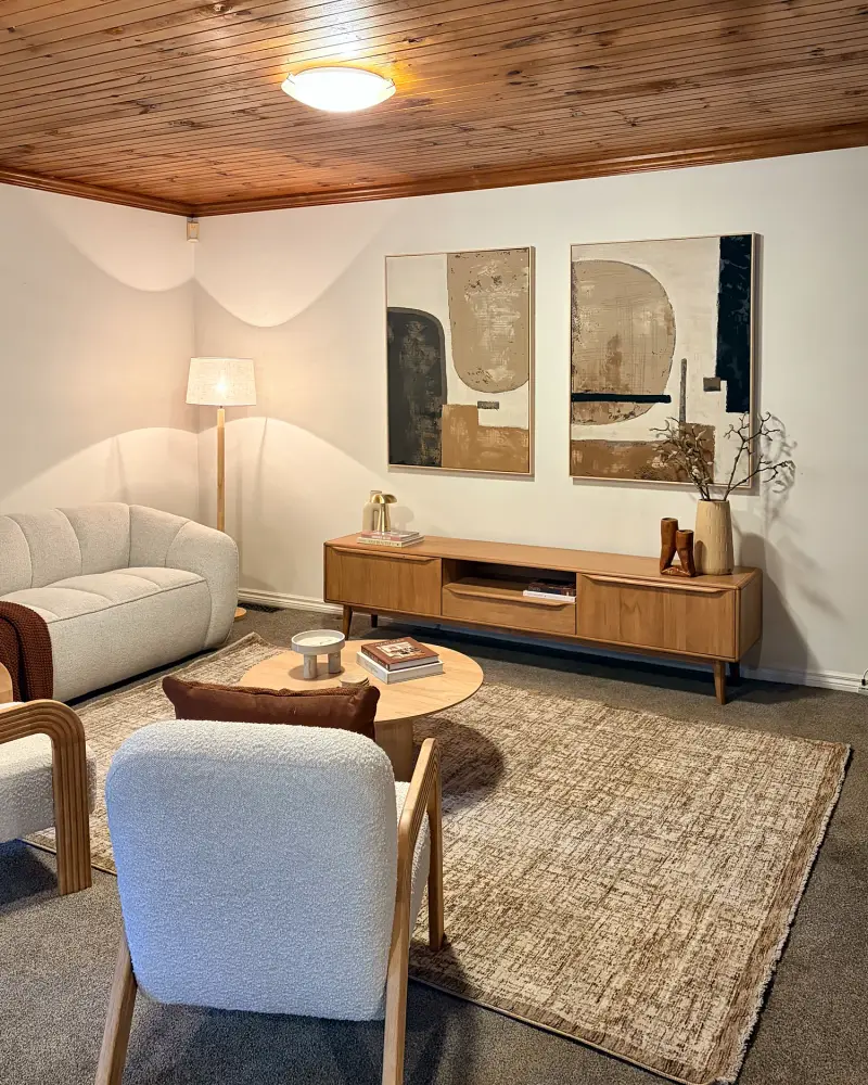 Living room with a timber-lined ceiling, cream sofa, boucle armchairs and round coffee table.