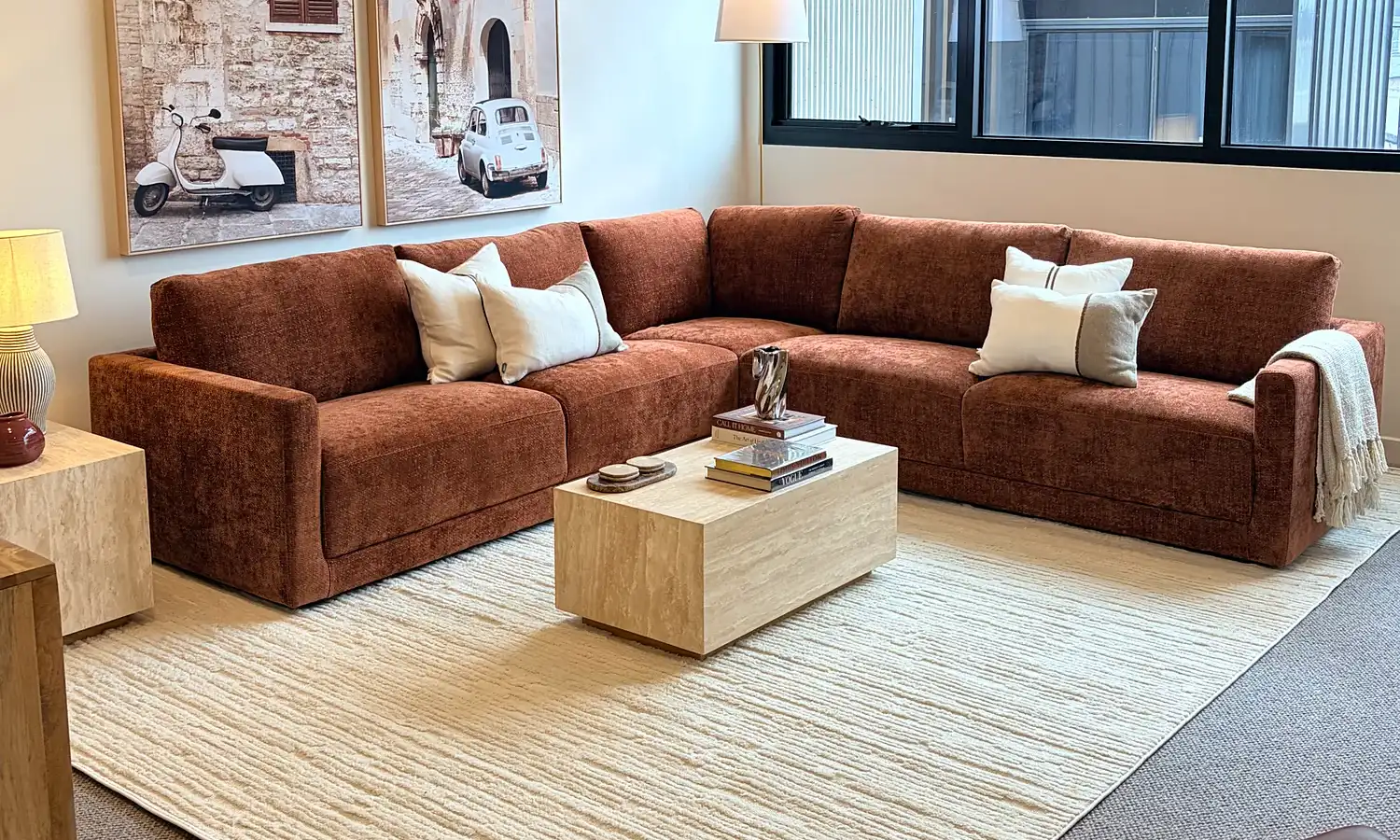 Living room with a rust modular sofa, cream rug and travertine coffee table.