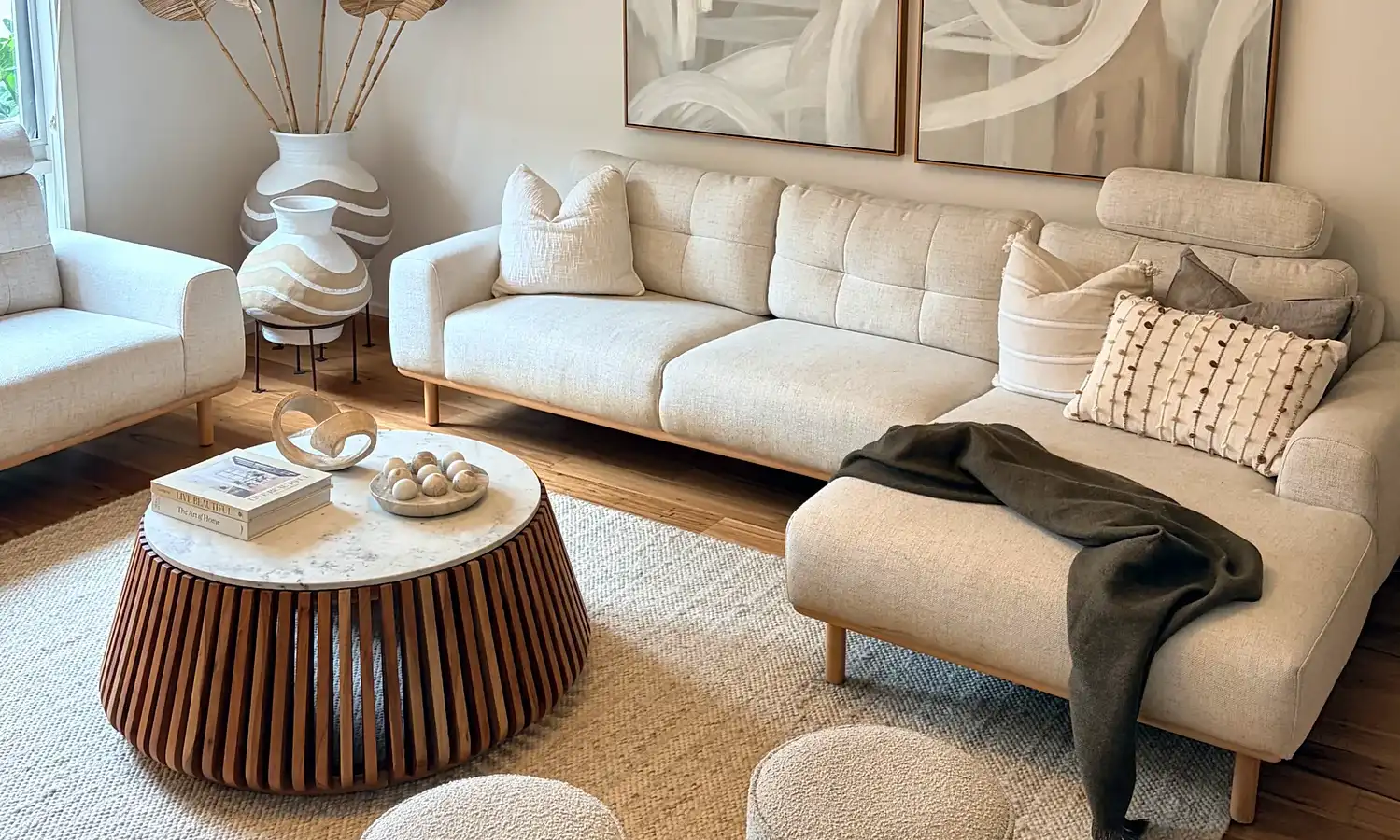 Living room with cream sofas, a round fluted timber coffee table, ottomans and abstract artwork.