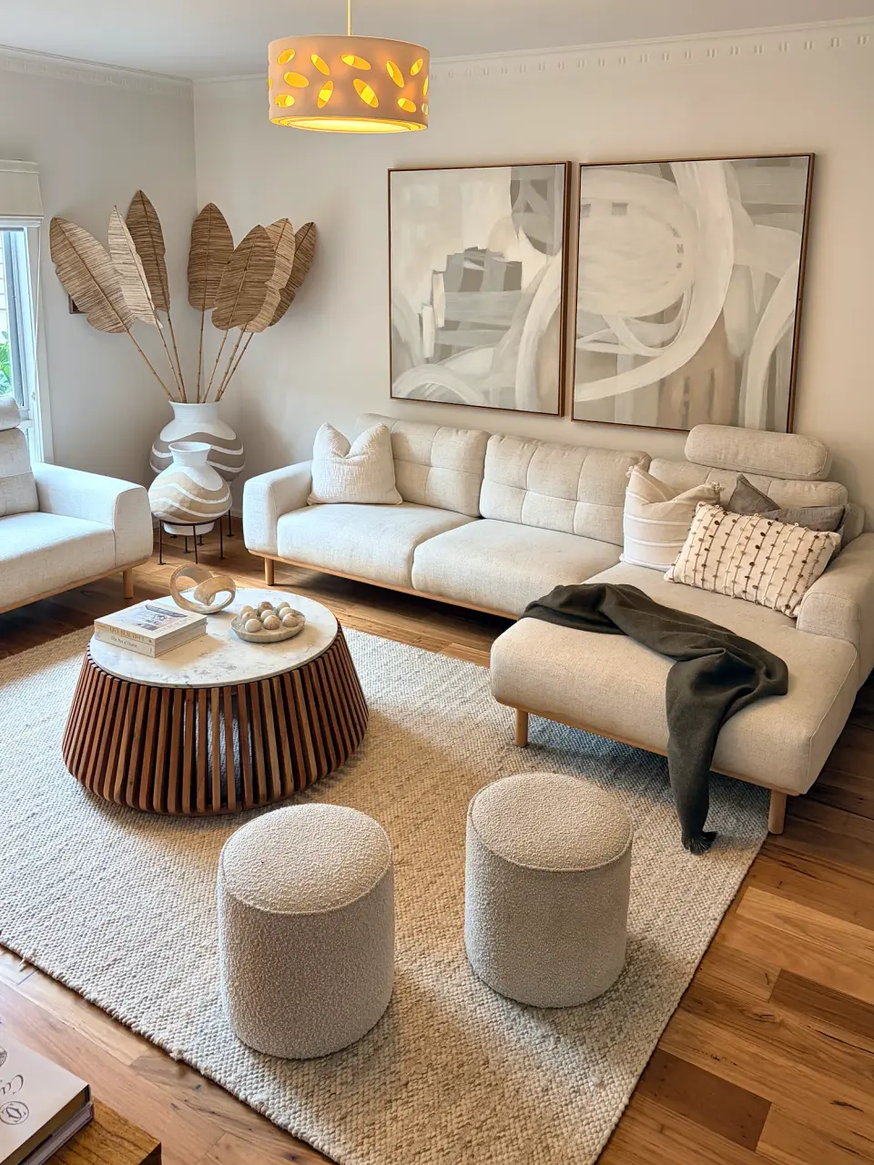 Living room with cream sofas, a round fluted timber coffee table, ottomans and abstract artwork.