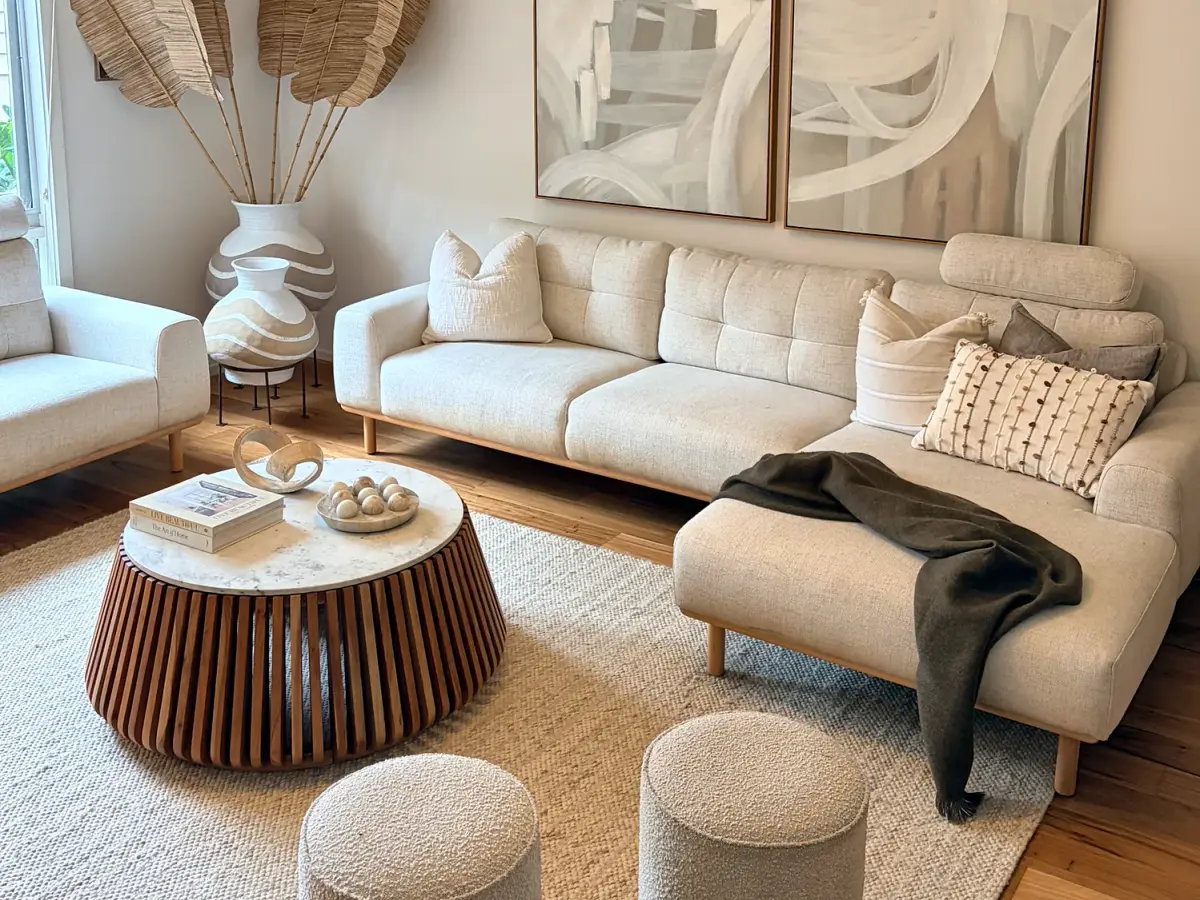Living room with cream sofas, a round fluted timber coffee table, ottomans and abstract artwork.
