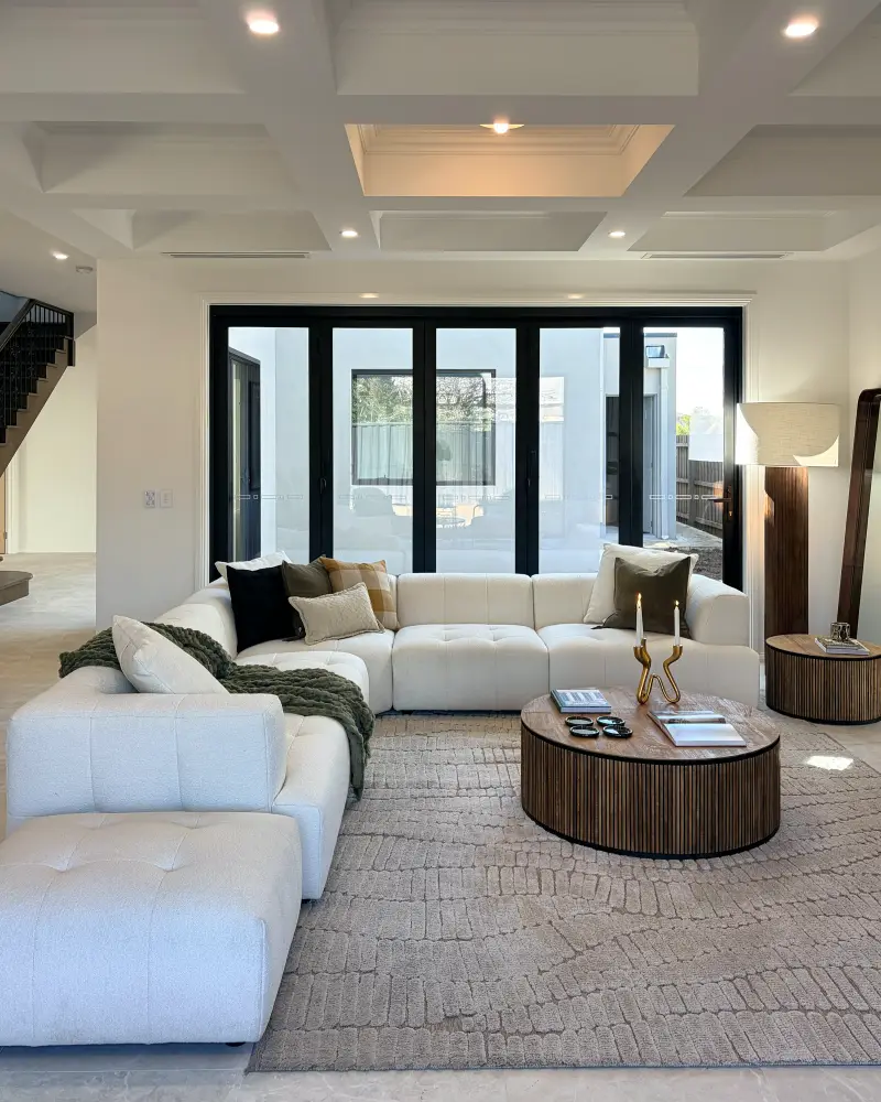 Open living area with a cream modular sofa, round fluted timber coffee table and coffered ceiling.