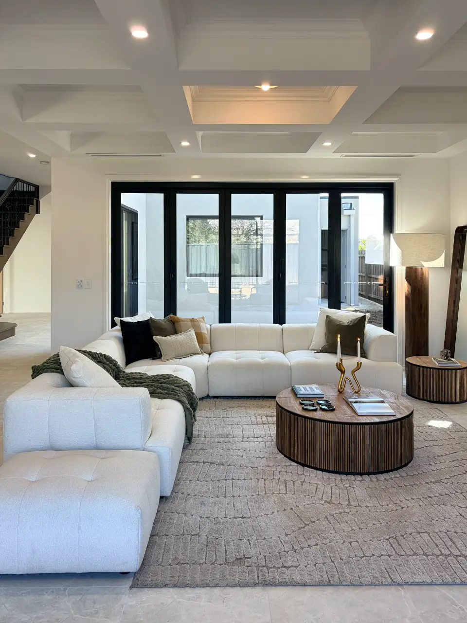 Open living area with a cream modular sofa, round fluted timber coffee table and coffered ceiling.