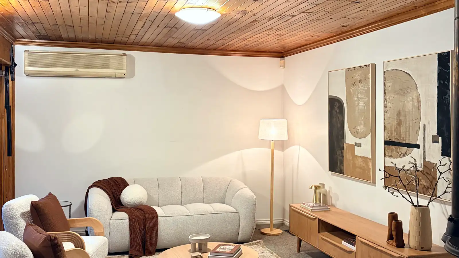 Wide view of the living room with cream armchairs, a timber entertainment unit and rug.