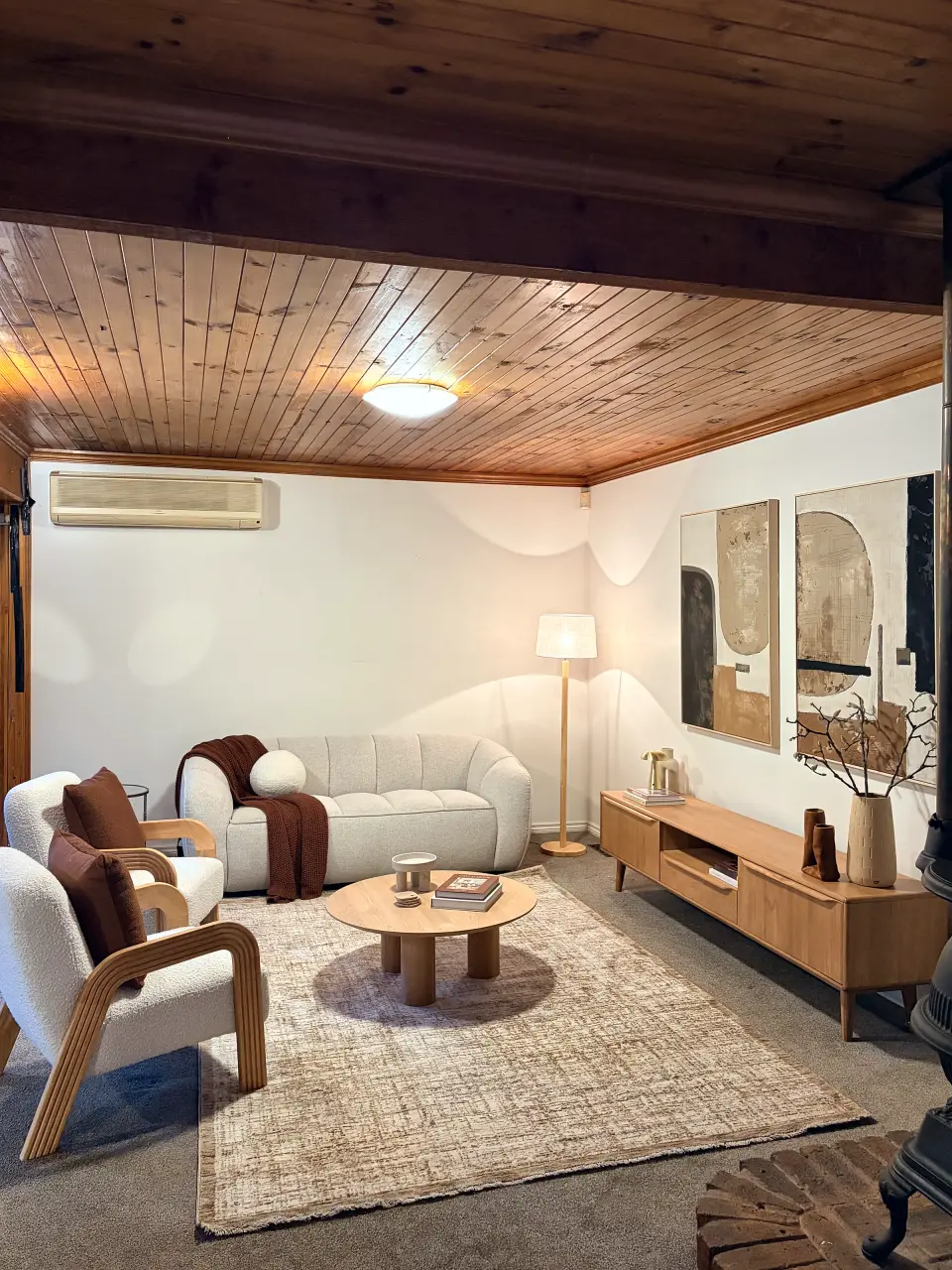 Wide view of the living room with cream armchairs, a timber entertainment unit and rug.