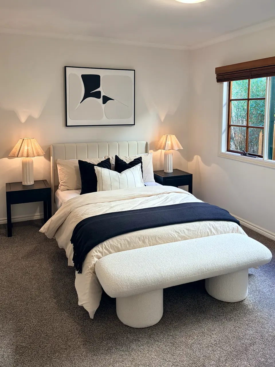 Bedroom with a cream bedhead, black and white bedding, boucle bench and abstract artwork.