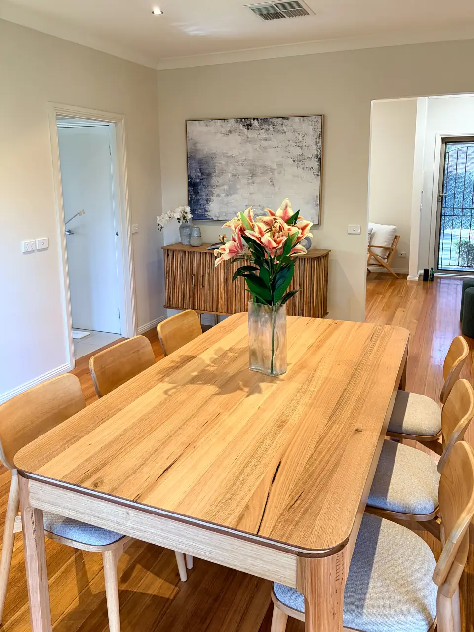 Timber dining table with fresh flowers, looking toward the sideboard.