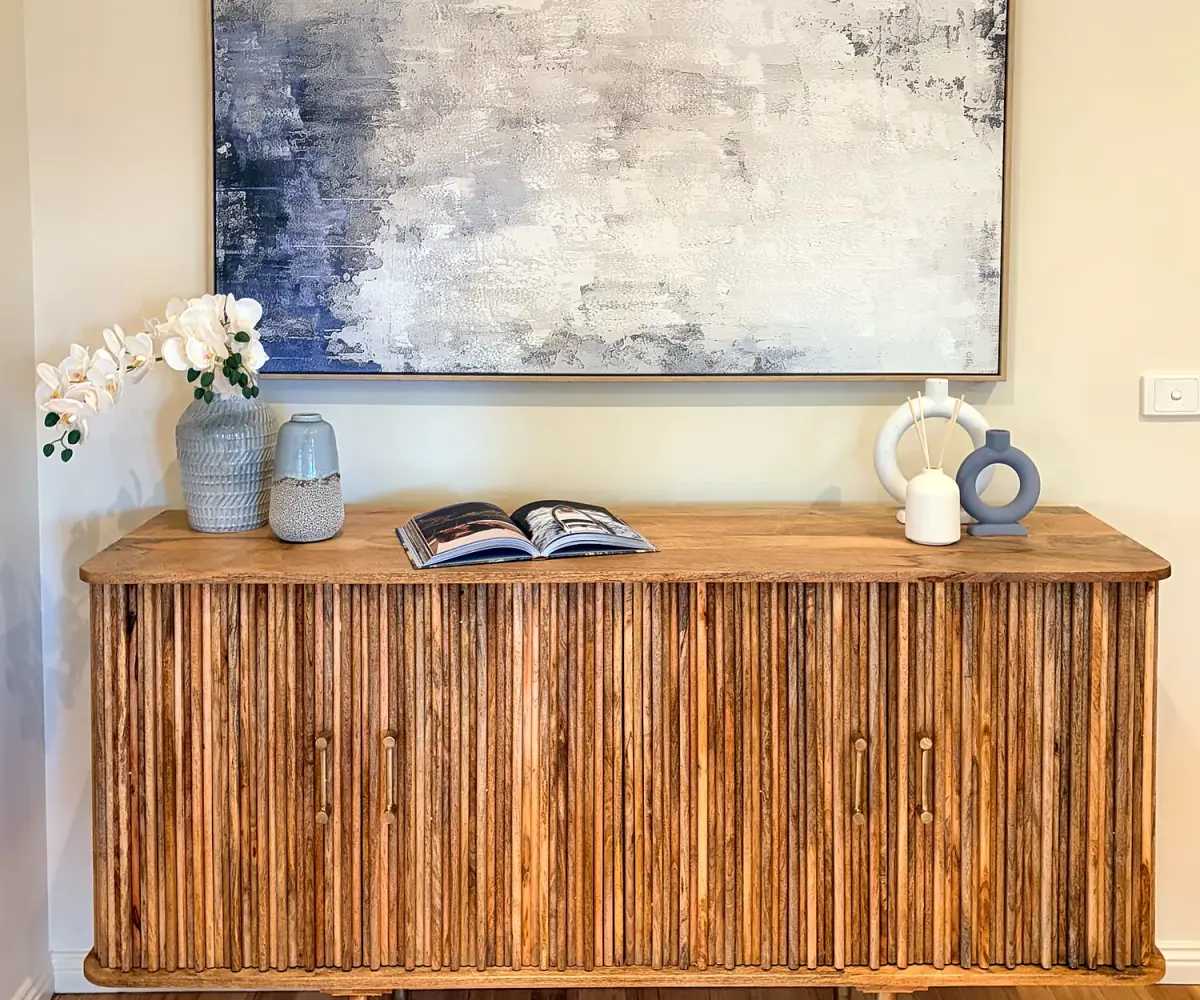 Fluted timber sideboard below a large blue and white abstract artwork.