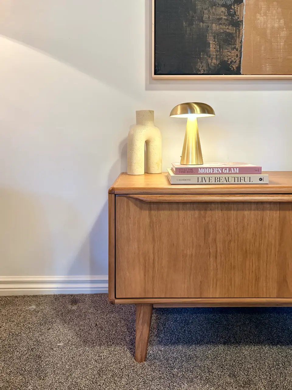 Timber sideboard with a brass dome lamp, ceramic vases and abstract artwork.