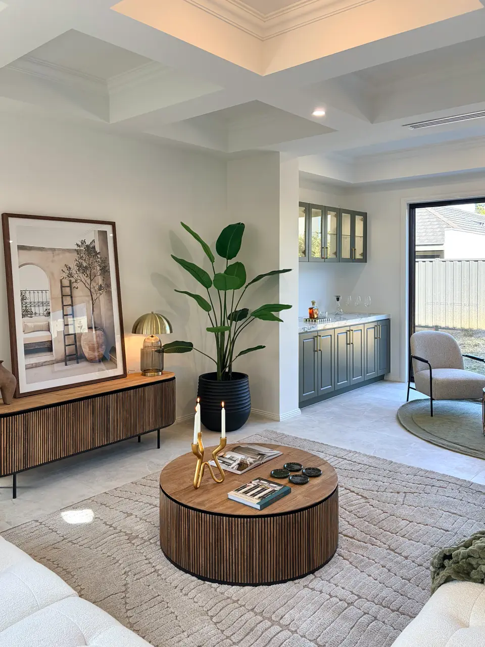Fluted timber sideboard, framed artwork, large plant and round coffee table in the living area.