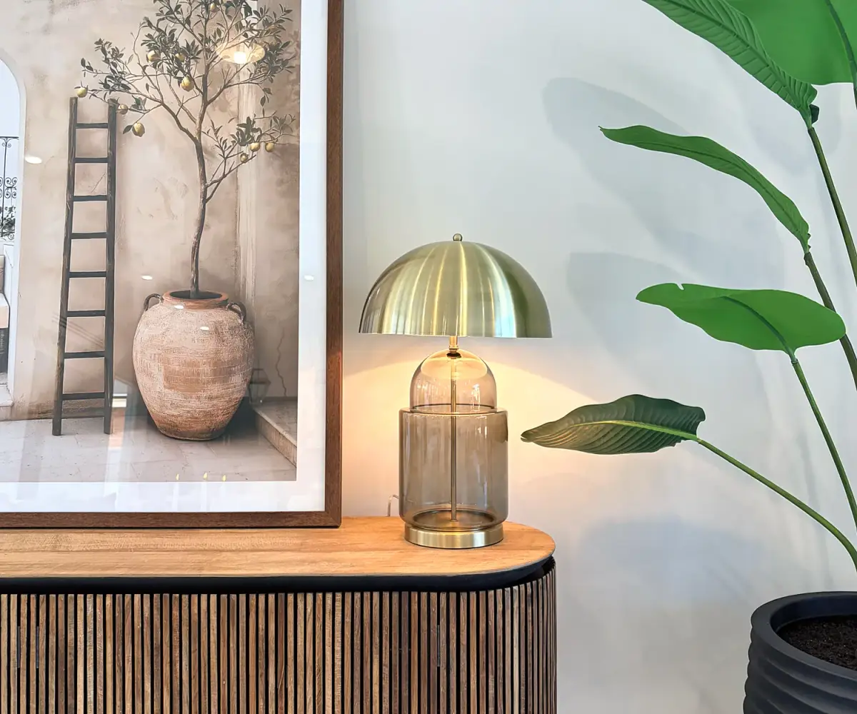Fluted timber sideboard with a brass dome lamp, framed artwork and a large plant.