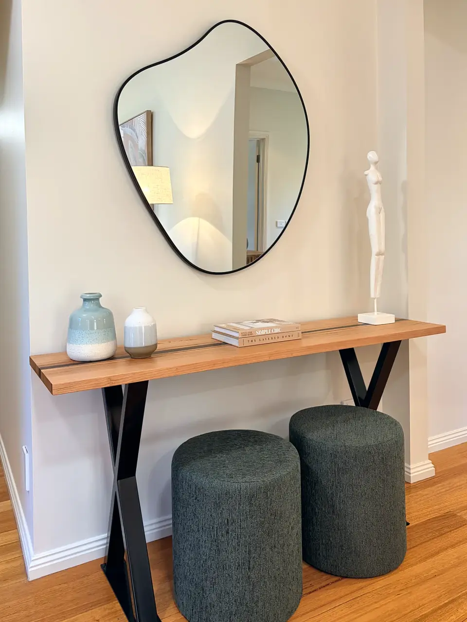 Entry console with an organic-shaped mirror and two charcoal ottomans.