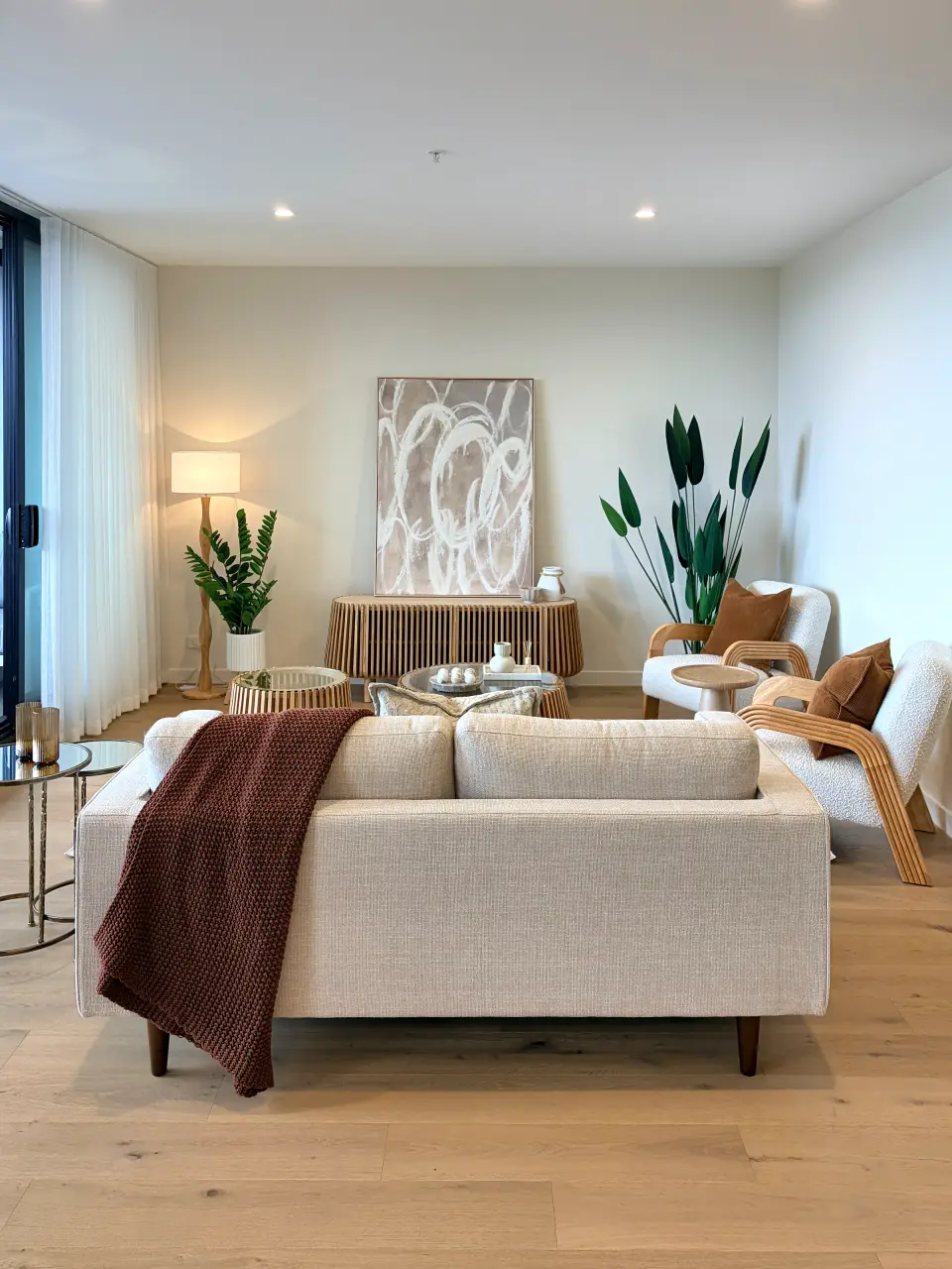 Cream sofa with a rust throw on timber floors, with plants and artwork behind.