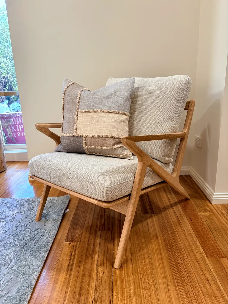 Timber-framed armchair with cream cushions on a patterned rug.