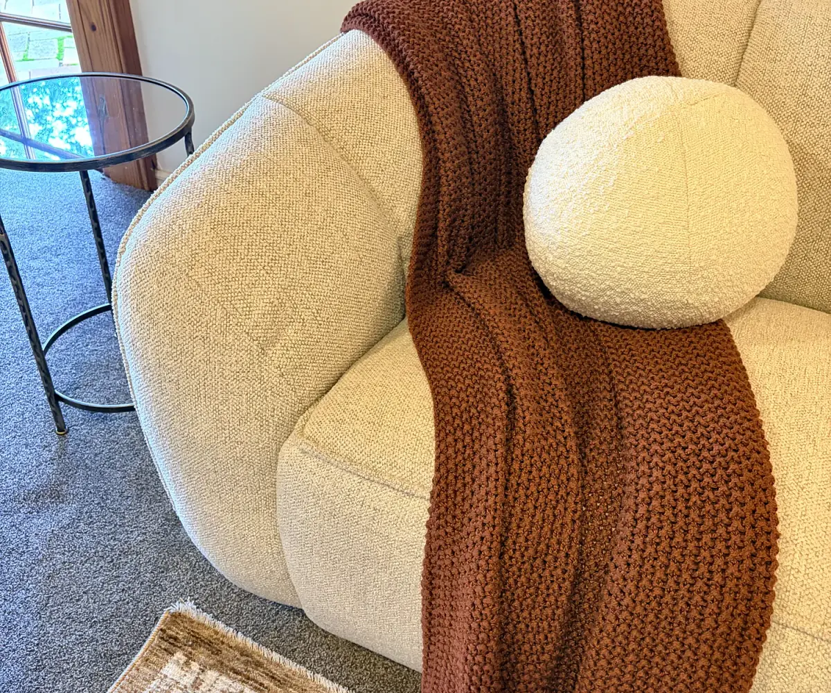 Boucle armchair with a rust knit throw and round cushion.