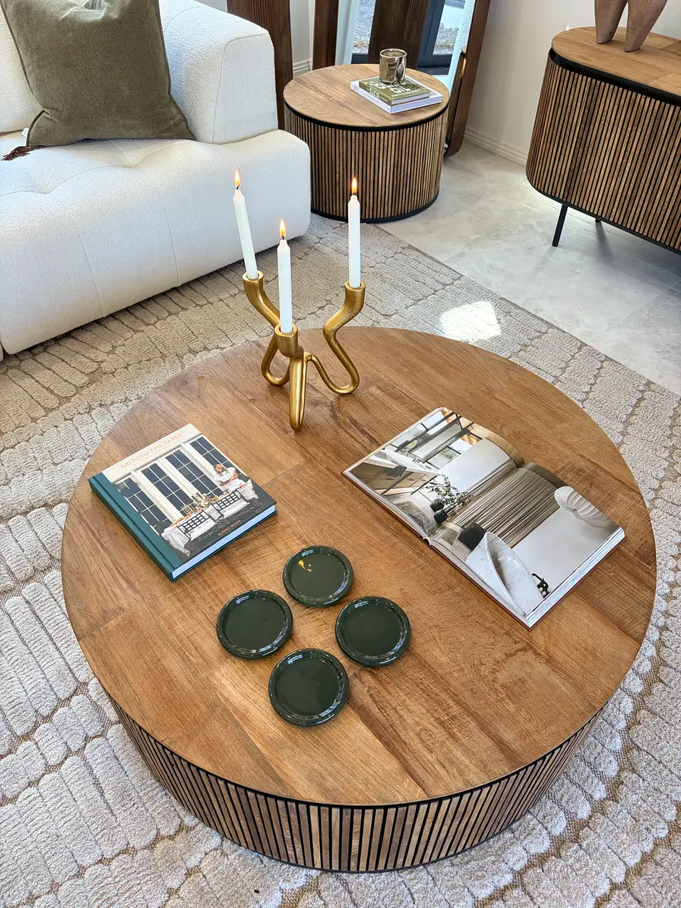 Round fluted timber coffee table styled with a brass candle holder, books and green coasters.