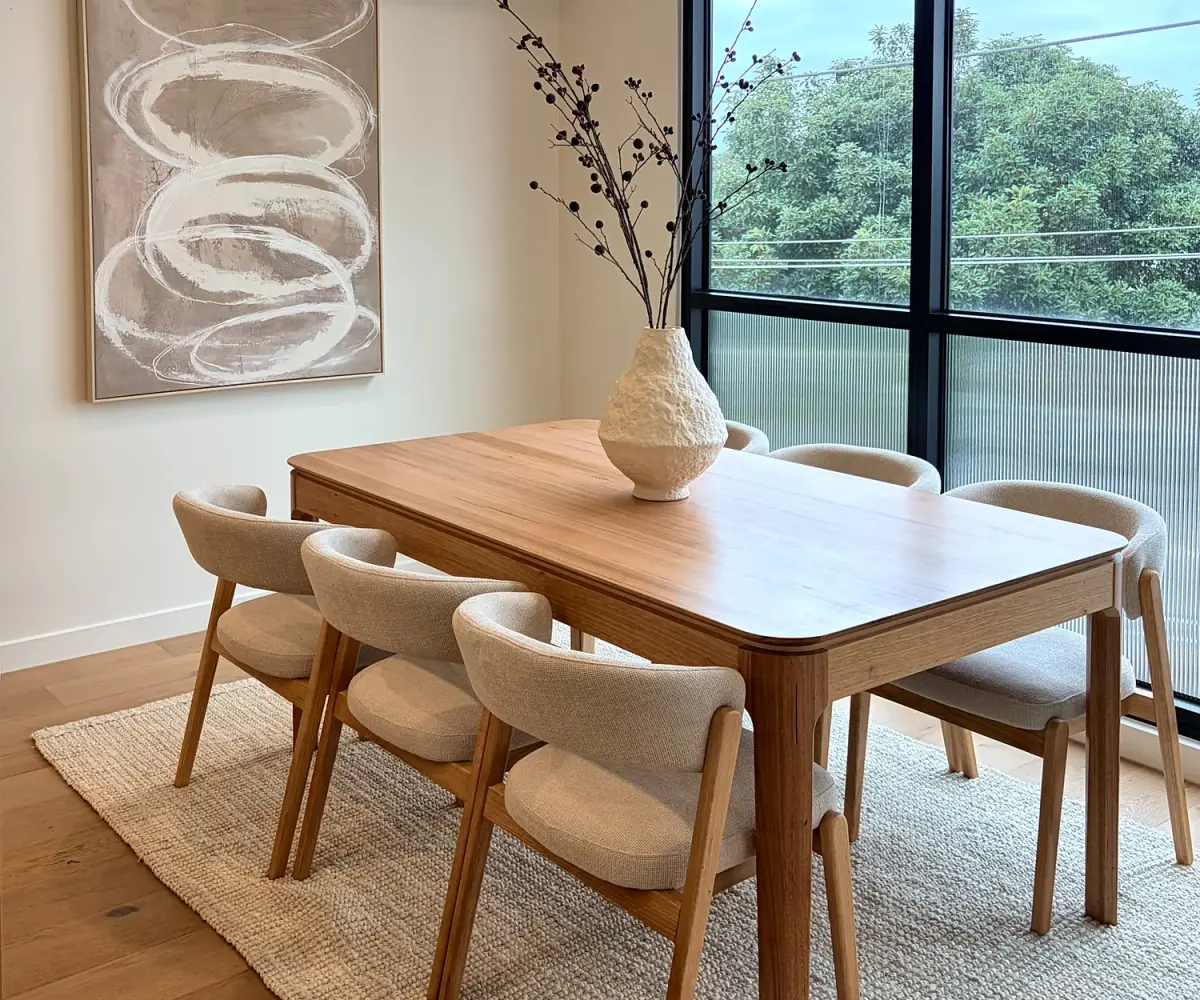 Dining area with a timber table, six curved cream chairs and abstract artwork.