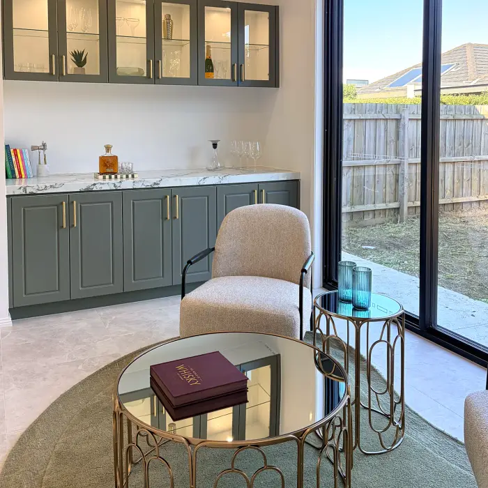 Sitting area with sage green cabinetry, a boucle chair and glass-topped side tables.