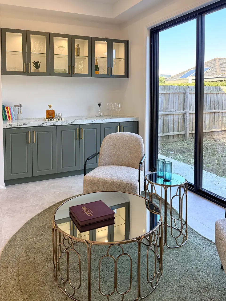 Sitting area with sage green cabinetry, a boucle chair and glass-topped side tables.