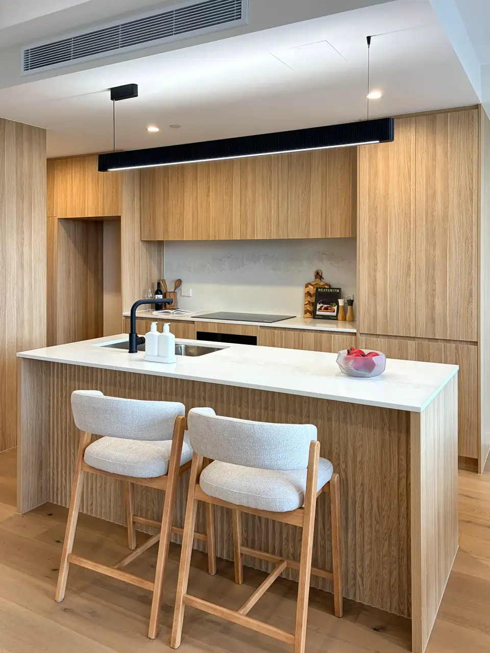 Kitchen island with two cream bar stools and timber joinery.
