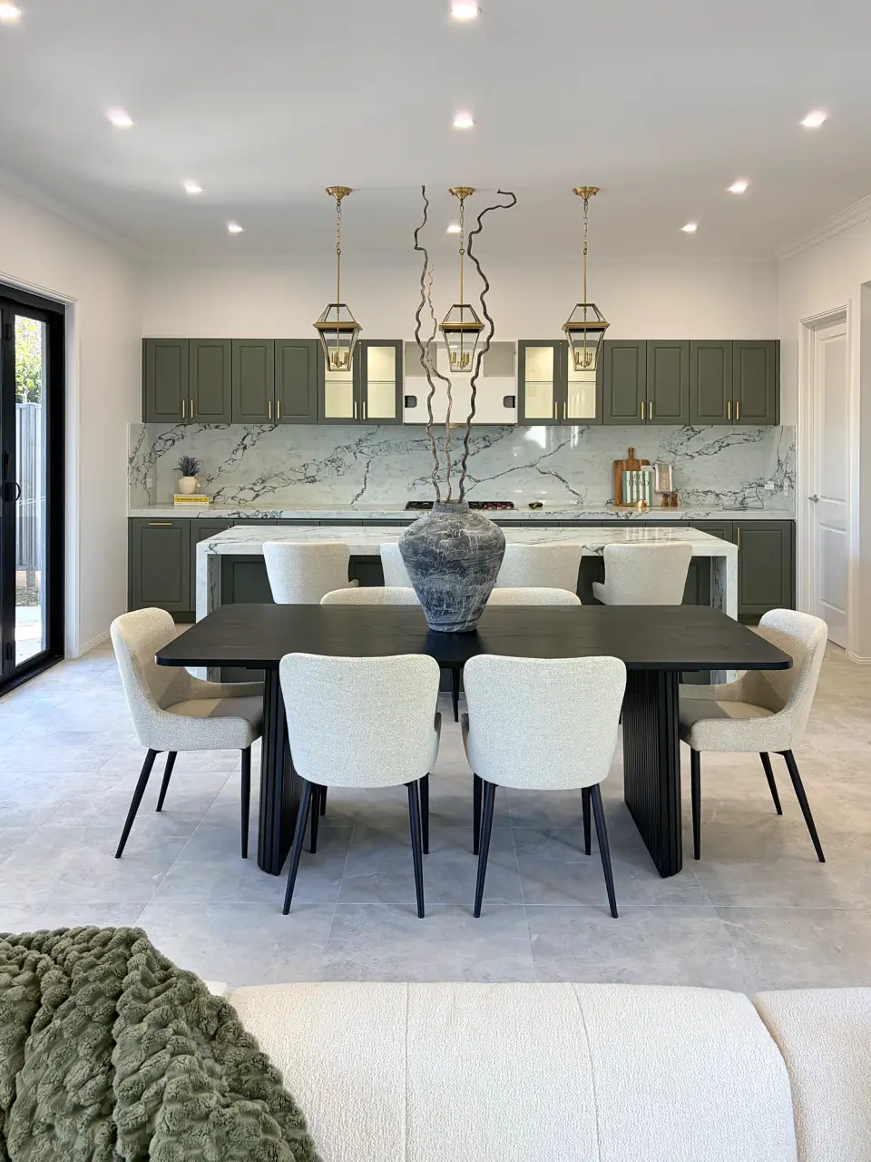 Dining table under pendant lights with the sage green kitchen behind.