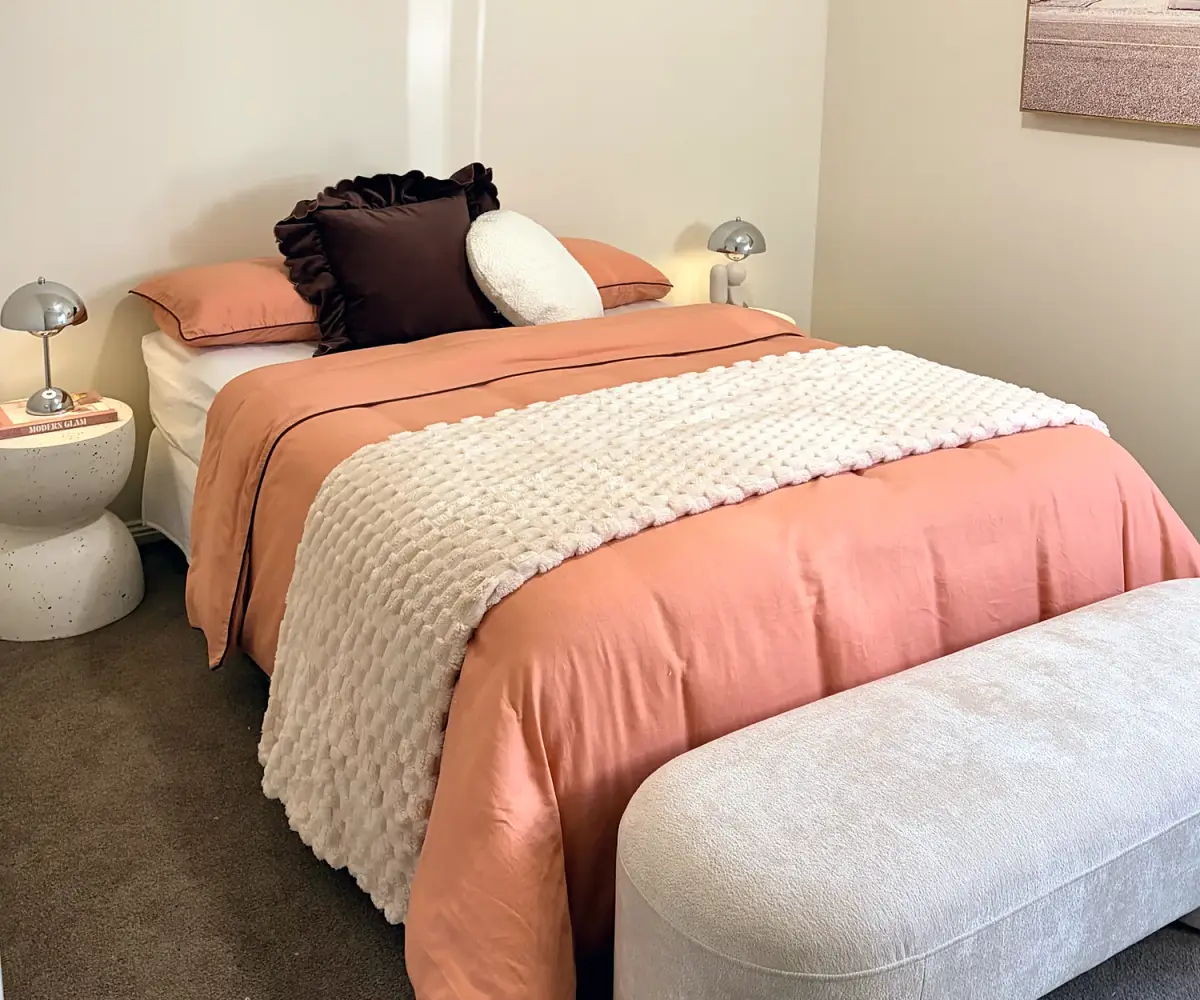 Bedroom with coral and cream bedding and a boucle bench.