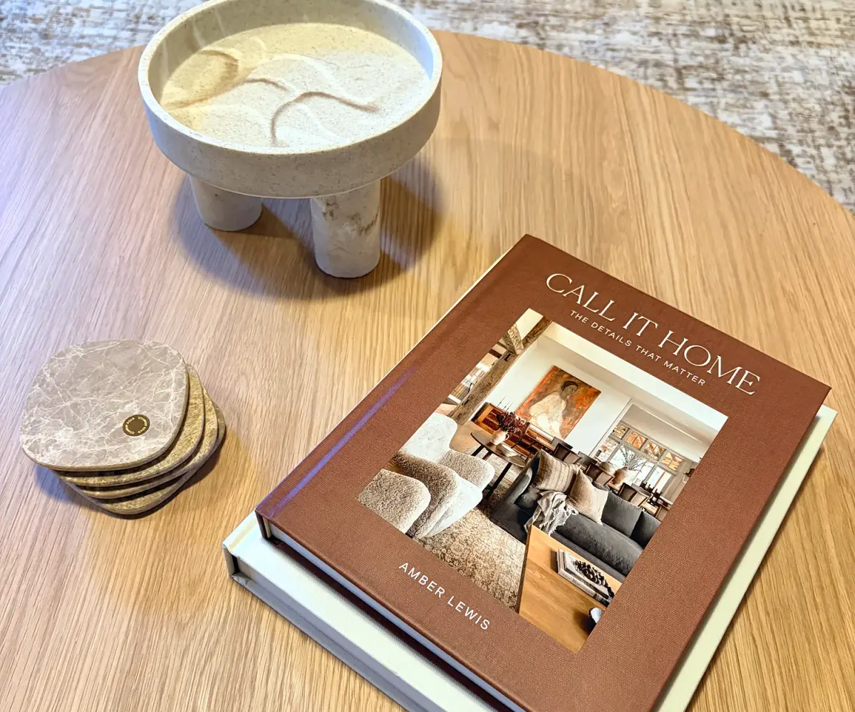 Round timber coffee table with a ceramic bowl, stone coasters and a design book.