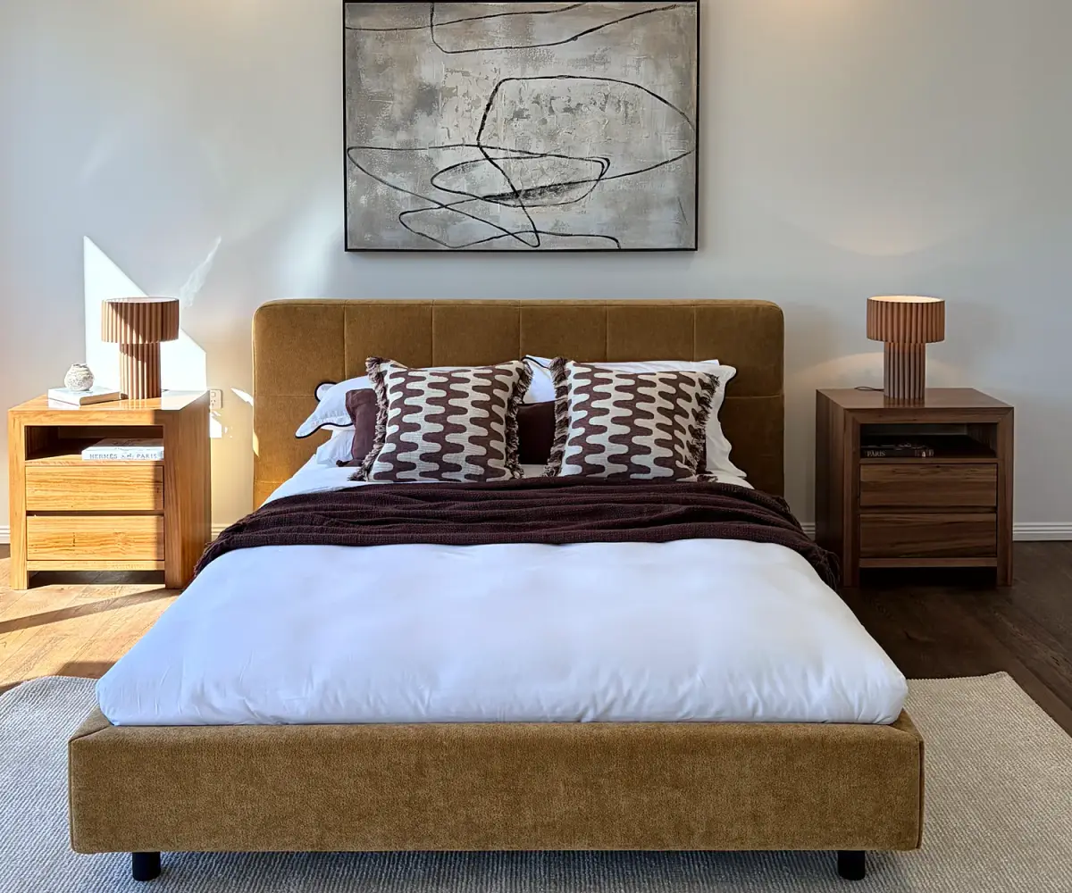 Bedroom with a mustard upholstered bed, timber bedside tables and abstract artwork.