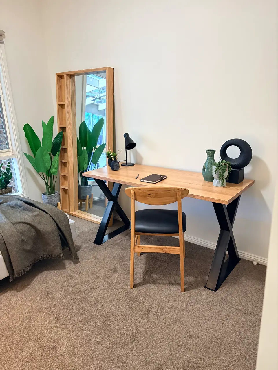 Study with a timber desk, black chair, mirror and plant.