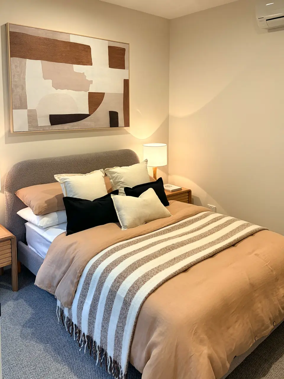 Bedroom with striped caramel bedding, black and cream cushions and abstract artwork.
