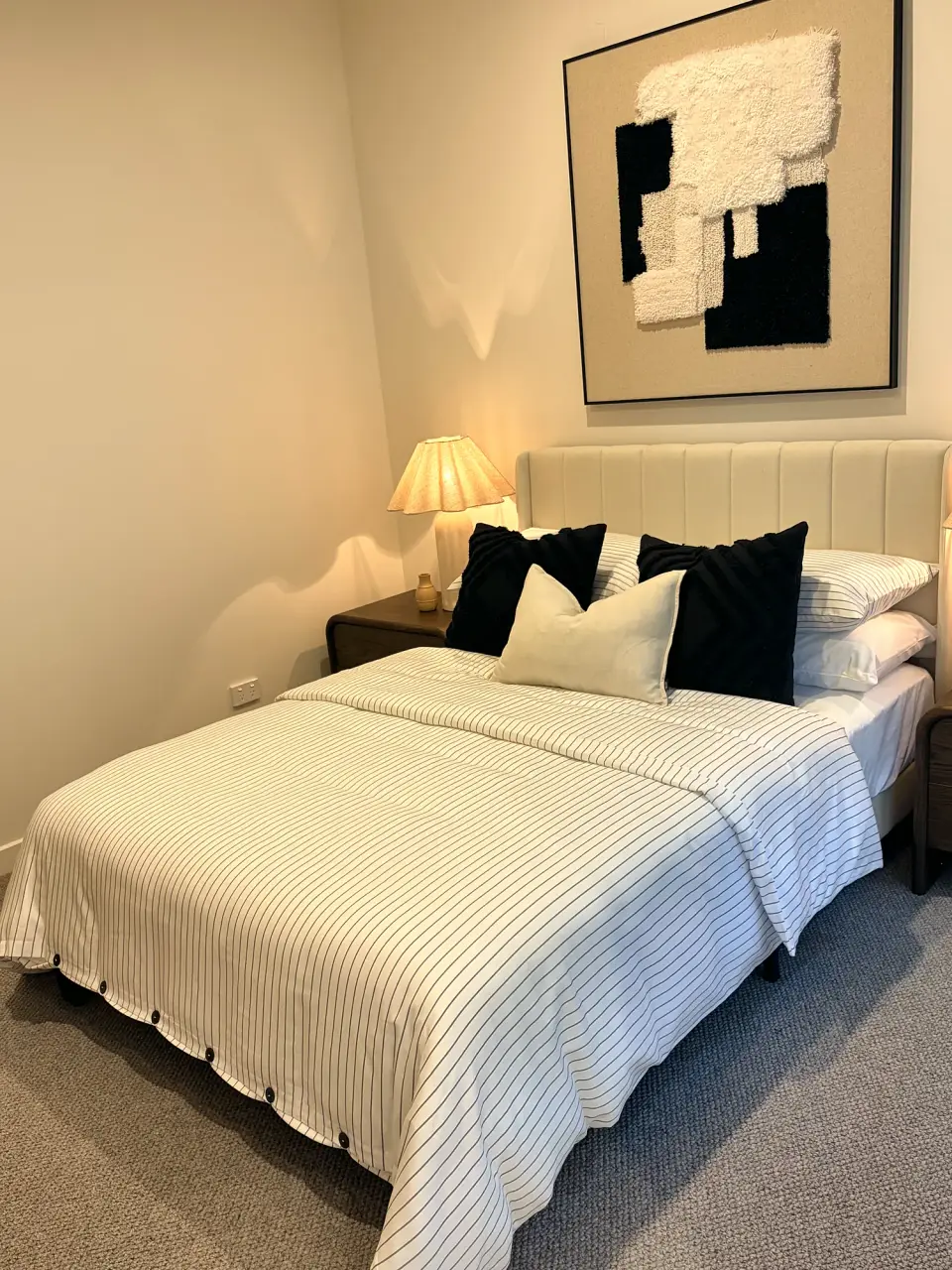 Bedroom with white striped bedding, black cushions and textured black-and-white artwork.