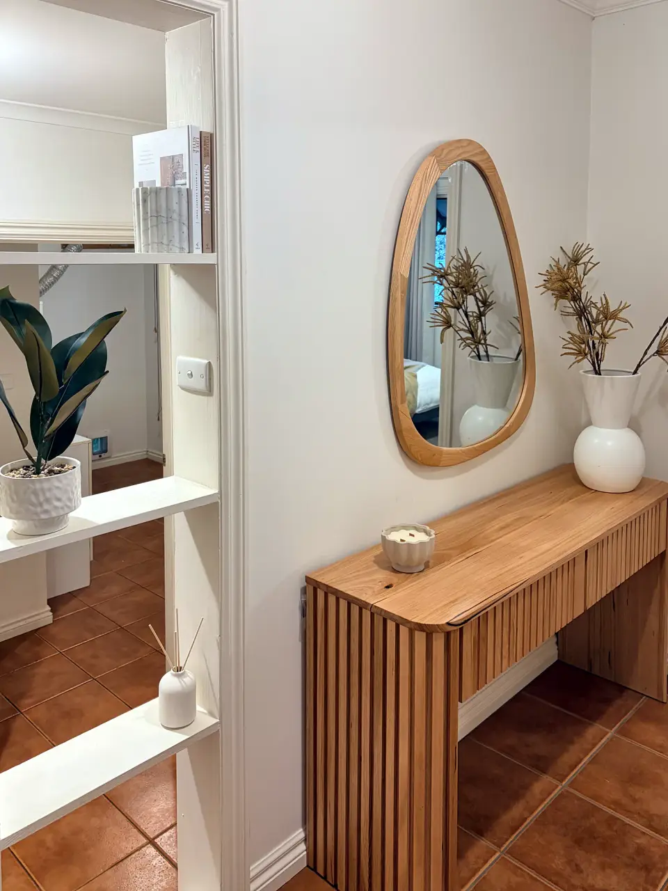 Hallway console with an organic-shaped mirror, vase and plant.