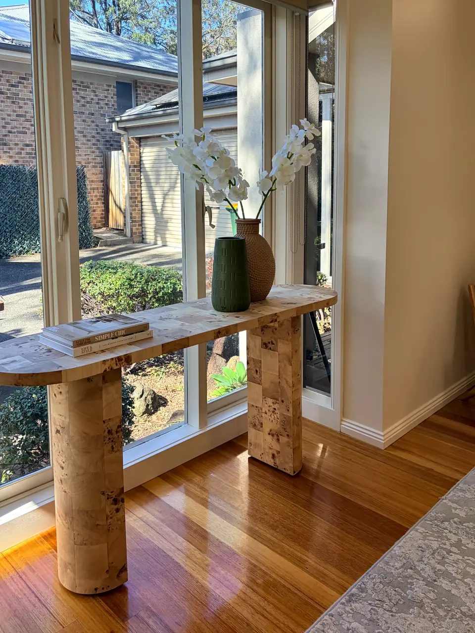 Burl timber console table with orchids beside a window.
