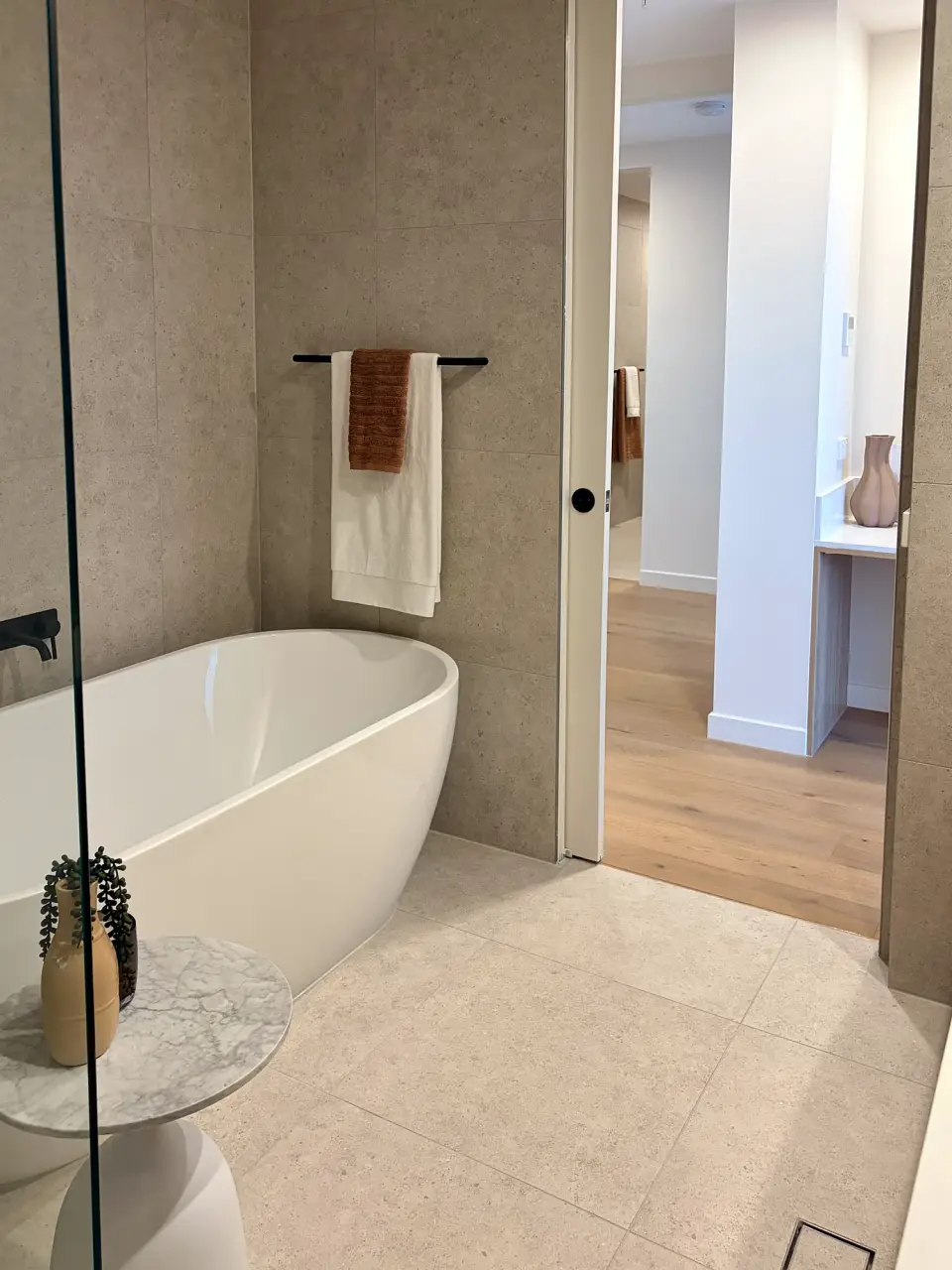 Bathroom with a freestanding bath, side table and rust-coloured towel.