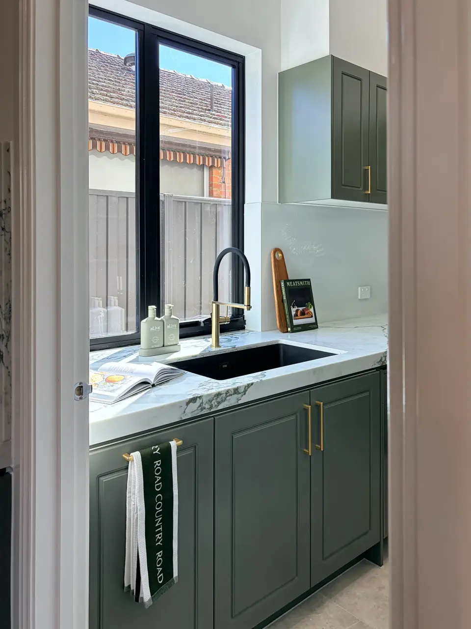 Sage green cabinetry with a black sink and marble benchtop.