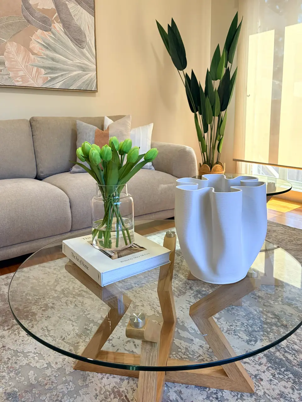 Glass coffee table with tulips and a white sculptural vase, grey sofa behind.